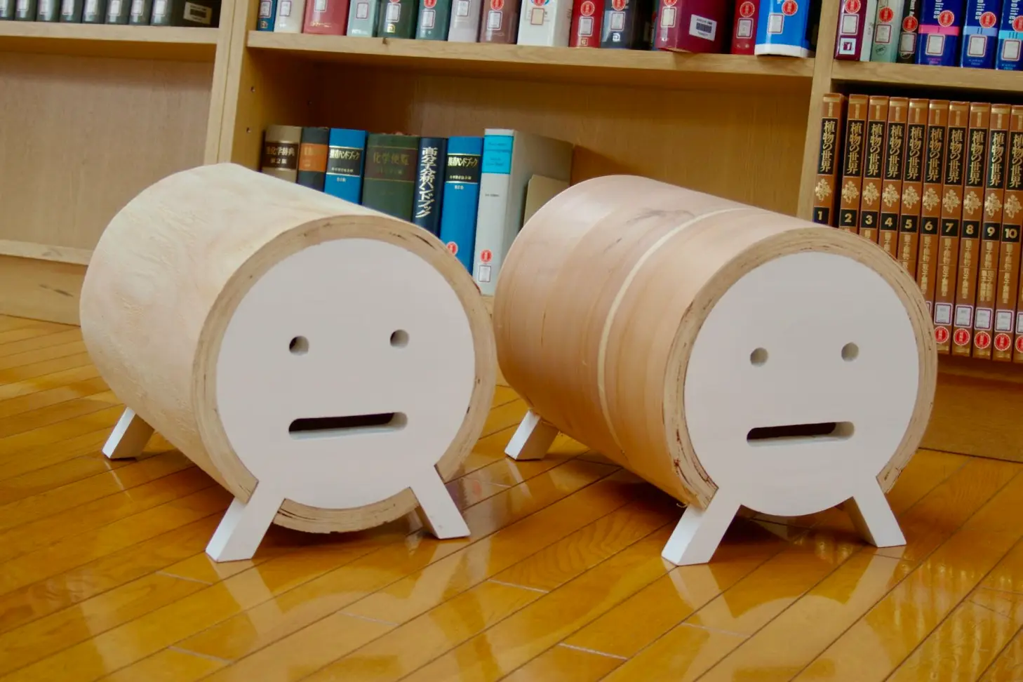 Two wooden cylindrical objects with simple facial expressions placed on the floor