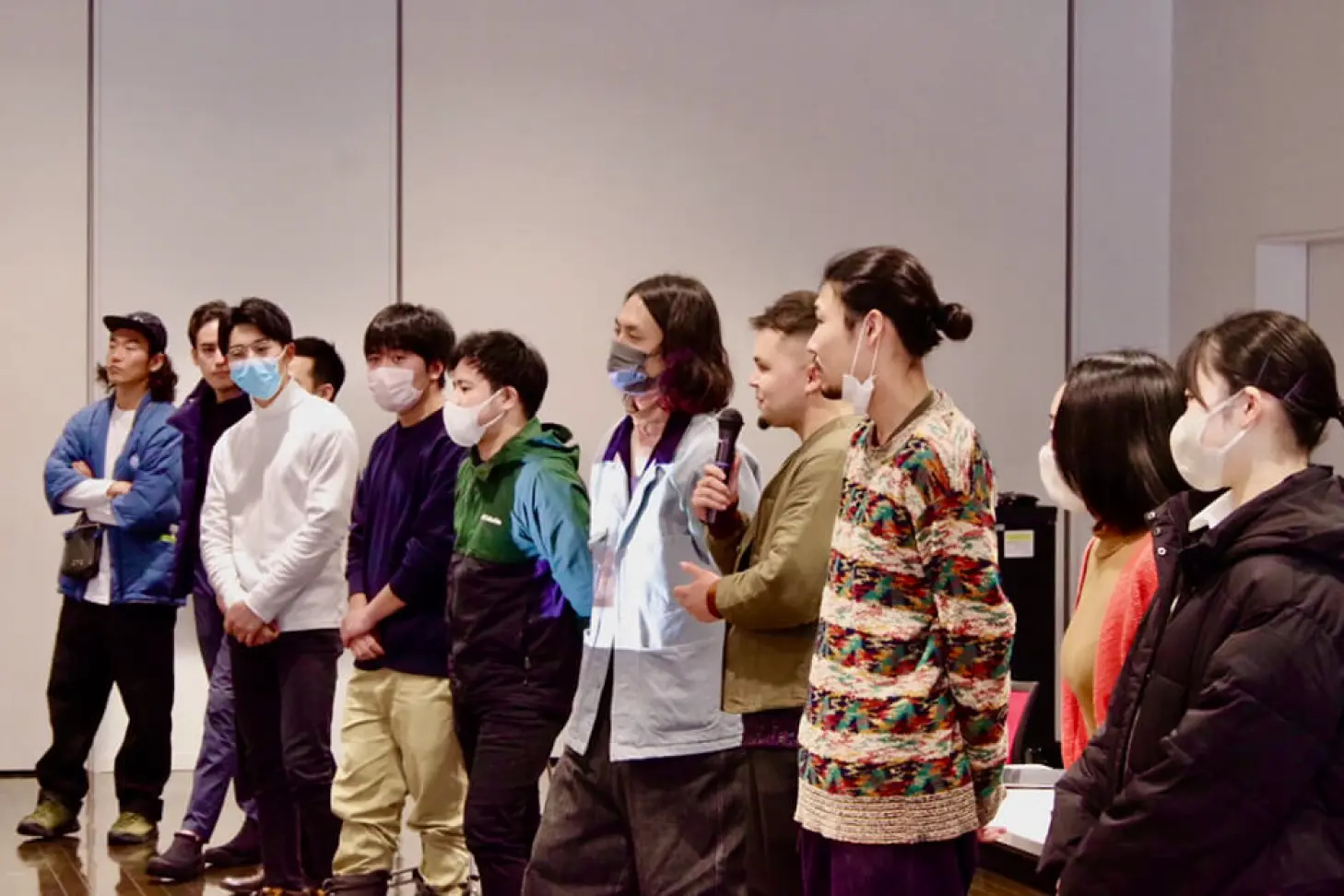 Several people standing in a row, some speaking into microphones, showing an event or workshop scene